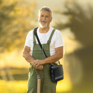 Man wearing nasal cannula and holding a shovel, using the Inogen One G5 Carry Bag outdoors.